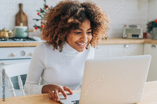 Concentrated and excited dark skinned young buyer with trendy hair looks in laptop smiles and enjoys online shopping closeup