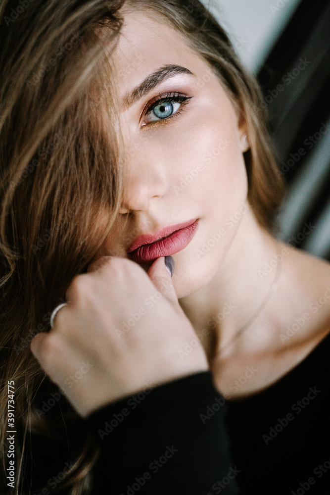 Portrait of a beautiful girl with light brown long hair in a black t-shirt and jeans on the stairs in the house. Beautiful blue eyes Portrait of a beautiful girl with light brown long hair in a black t-shirt and jeans on the stairs in the house. Beautiful blue eyes