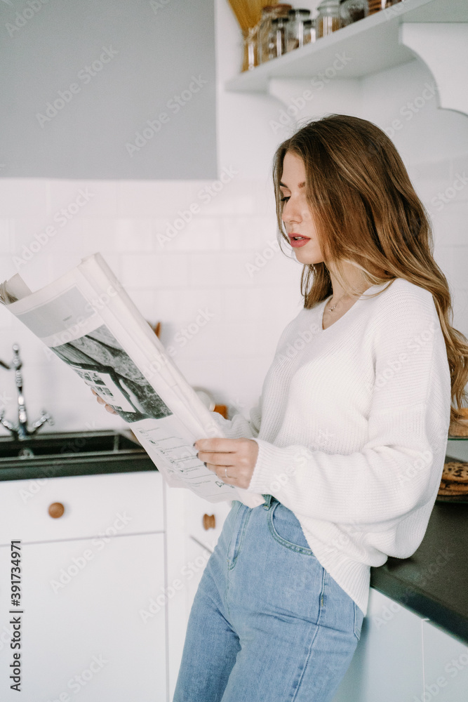 Beautiful blonde girl reads a newspaper in the morning in the kitchen Beautiful blonde girl reads a newspaper in the morning in the kitchen