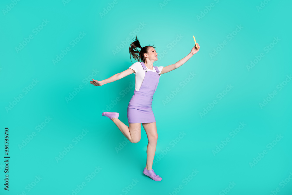 Full length body size side profile photo of happy girl with tails jumping taking selfie smiling isolated on vibrant teal color background