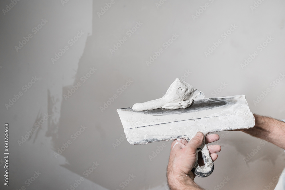 A construction worker puts white putty on a spatula from a bucket. Close-up A construction worker puts white putty on a spatula from a bucket. Close-up