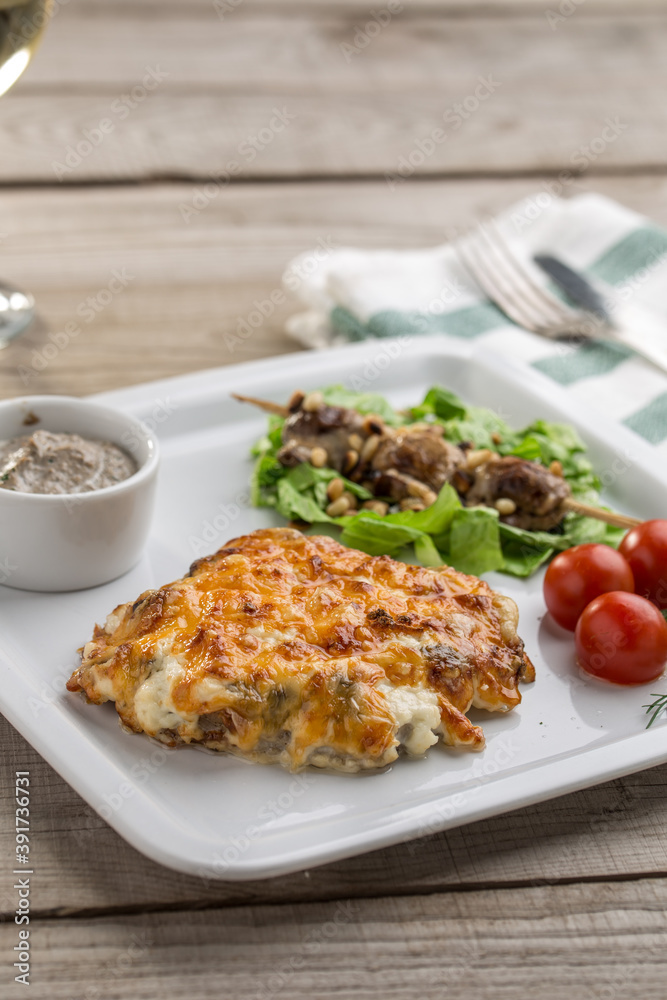 Baked pork with mushroom and mayo cheese sauce and fresh tomatoes on wooden table Baked pork with mushroom and mayo cheese sauce and fresh tomatoes on wooden table