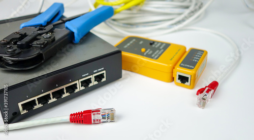 Network switch, ethernet cable, crimper and RJ45 cable tester isolated on white background.