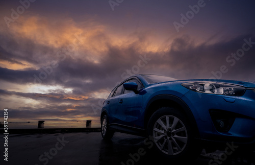 Luxury SUV car with raindrops. Front view new blue SUV car parked on concrete parking lot near sea beach with sunset sky. Electric vehicle concept. Road trip travel. Car covered with water drops.