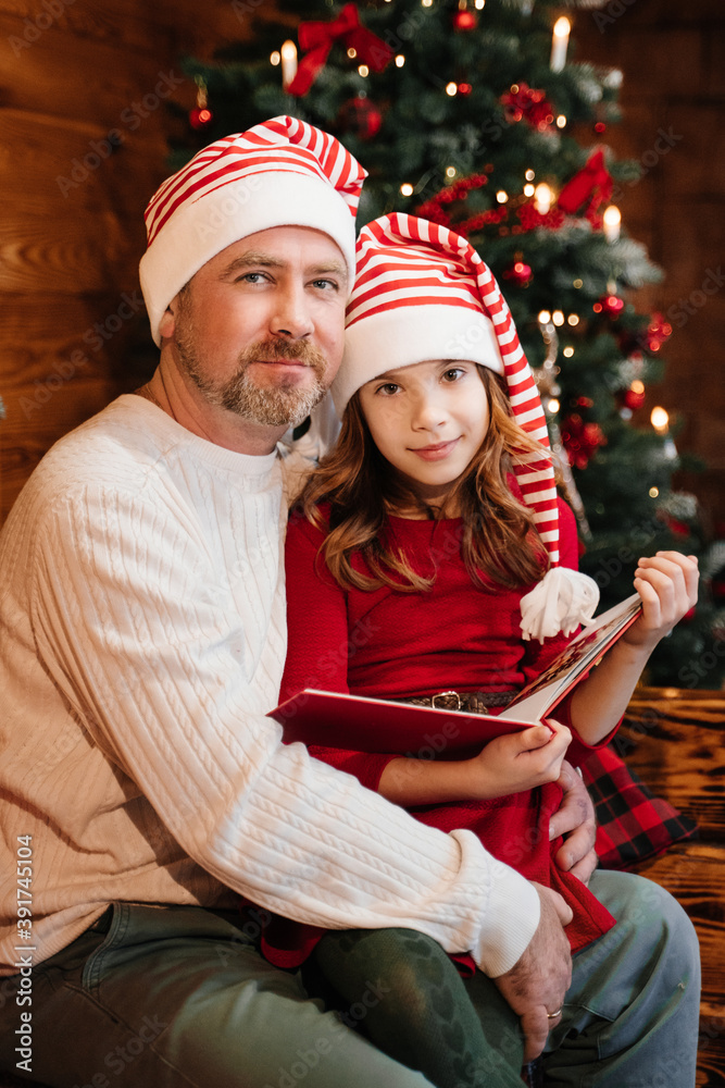 Dad is reading a book to his daughter. A girl in a red New Year's suit.