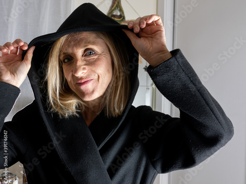 BLONDE SPANISH WOMAN DRESSED IN BLACK, WITH A HOOD IN THE ROOM OF HER HOUSE, WITH HANDS ON HER FACE AND HOOD LOOKING INSINUALLY AND INQUIRINGLY photo