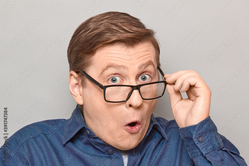 Portrait of shocked man peering over glasses at something unbelievable Portrait of shocked man peering over glasses at something unbelievable