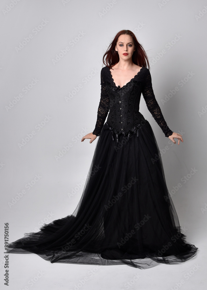 full length portrait of  woman wearing black gothic dress,  Standing pose  against a studio background.