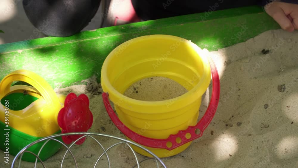 A child is playing in a sandbox with a toy bucket and a bailer