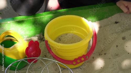 A child is playing in a sandbox with a toy bucket and a bailer