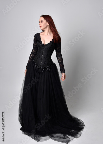 full length portrait of woman wearing black gothic dress, Standing pose against a studio background.