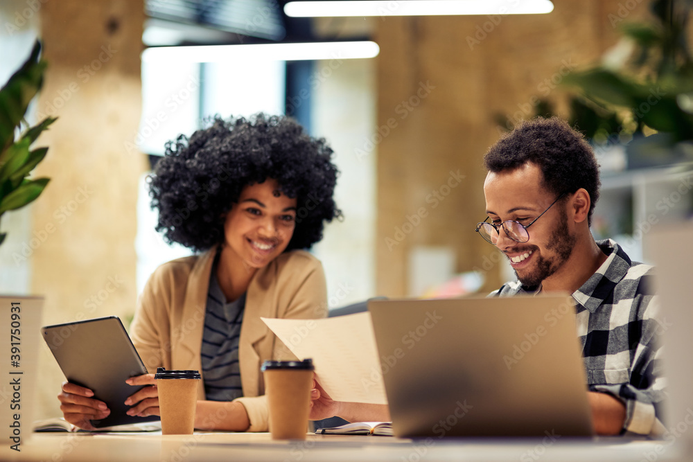 God job. Two young diverse coworkers analyzing sales report while working together in the office God job. Two young diverse coworkers analyzing sales report while working together in the office