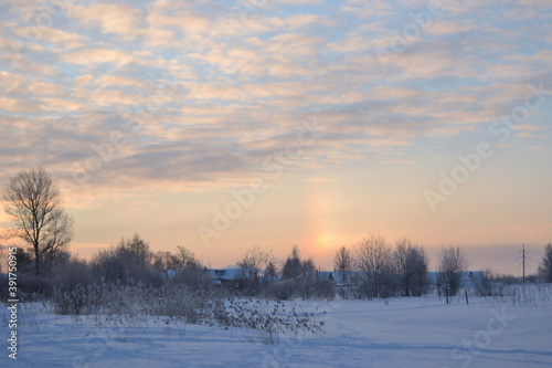 Frosty winter sunrise in the snow-white open spaces near the snow-covered Russian village. Winter nature landscape.