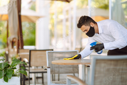 Wallpaper Mural Young Waiter in protective face mask and gloves sanitizing surfaces, cleaning the table with disinfectant spray in a restaurant. Covid- 2019. Torontodigital.ca