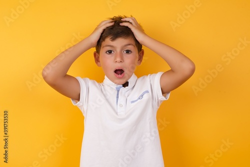 Horrible, stress, shock. Portrait emotional crazy Cute Caucasian little boy standing against yellow background  clasping head in hands. Emotions, facial expression concept.