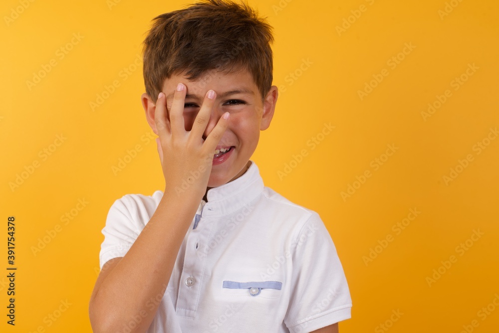Charismatic carefree joyful Young handsome Caucasian little boy standing against yellow wall likes laugh out loud not hiding emotions giggling hear funny hilarious joke chuckling facepalm.