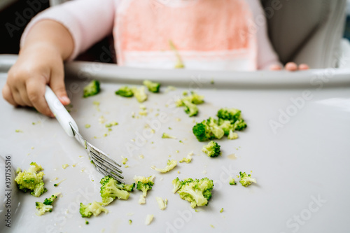 Little caucasian girl picking vegetables from a feeder in kitchen with fork, full vegan or vegetarian childhood healthy life, baby led weaning concept