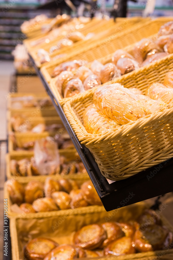 fresh golden breads with melted cheese wrapped in plastic wrap in wicker basket in bread department of supermarket