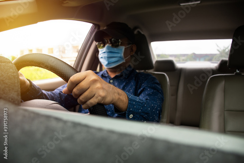 Blur male wearing a face mask, black glasses, and a black hat. Closeup a man driving hands to hold the steering wheel to control the car carefully While traffic congestion daylight. Blurred background © Mdisk