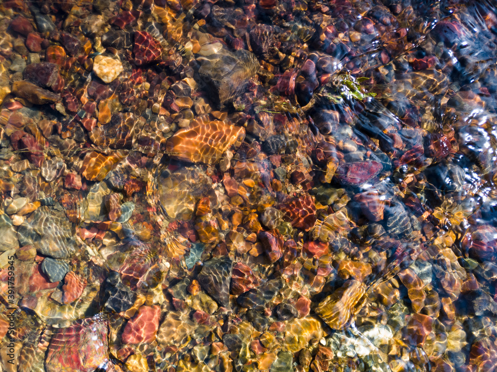 Obraz premium Detail from the creek, the shallow water flows over the colorful gravel and makes a pattern of refracting light during a sunny summer day.