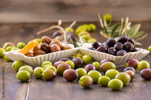 Green  black olives inside and outside in white bowl on wooden background.