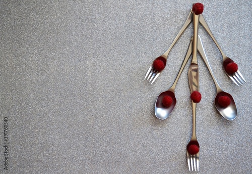 Christmas greeting for restaurants: Christmas tree consisting of steel spoons, forks and knives with raspberries as balls on a shiny silver background