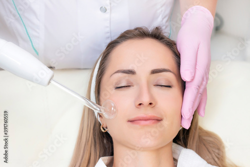 Cosmetologist performs a pulse current procedure for the face of a young woman.