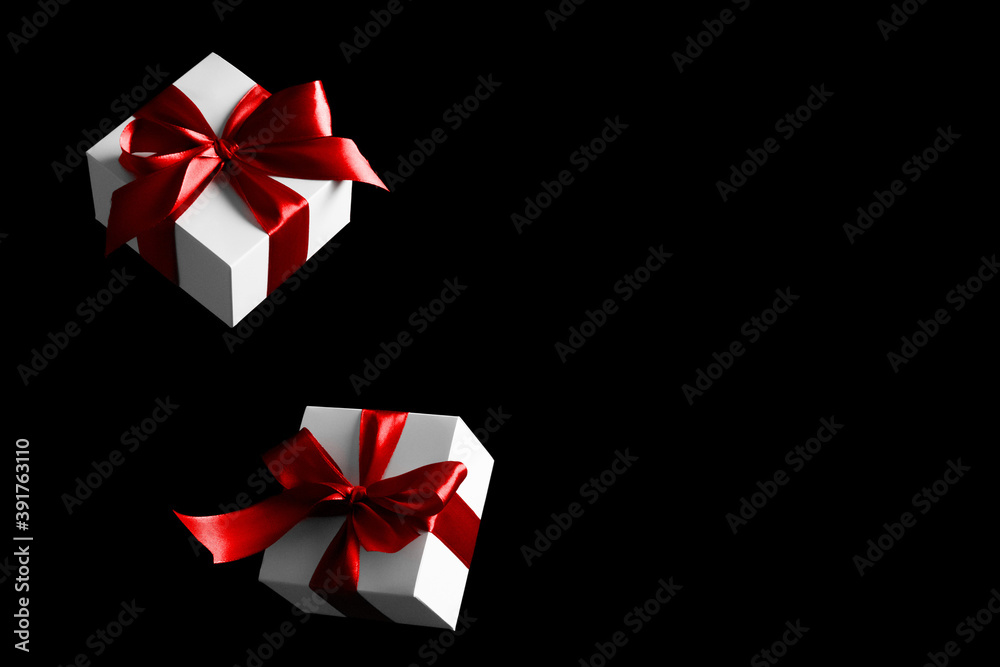 Black friday star. White gift box with red ribbon isolated on black background in Black Friday concept. Winter flying composition with copy space.