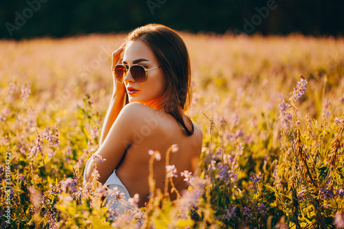 Girl in glasses with a bare back in a field at sunset