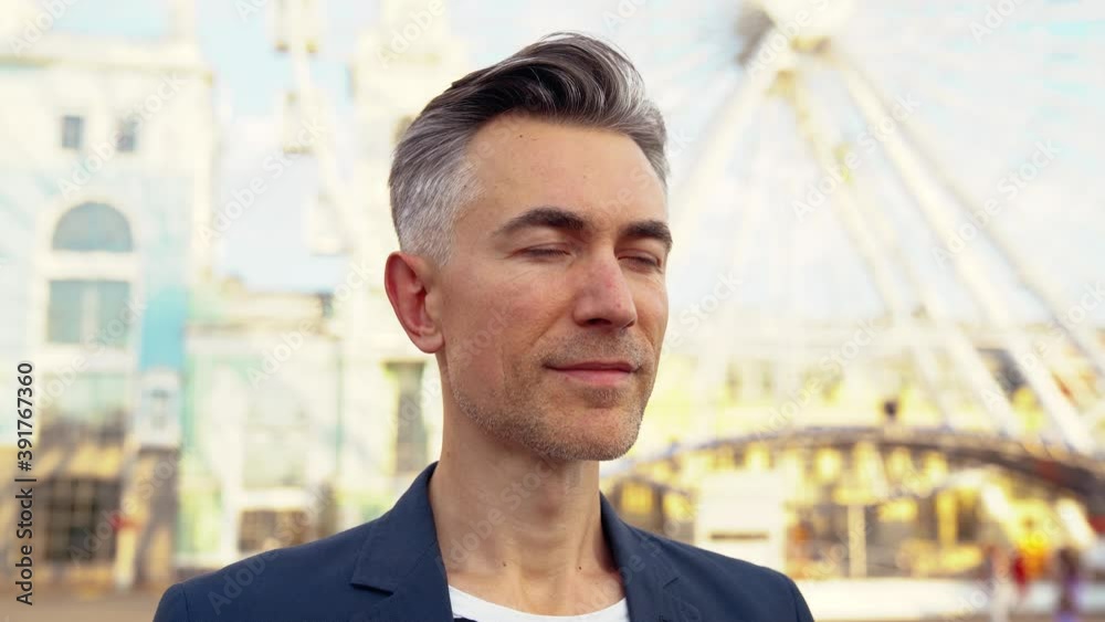 Portrait shot of middle-aged serious attractive Caucasian businessman looking straight at camera and at side while standing on town street at ferris wheel. Outdoors. Close up of face of stylish man. Portrait shot of middle-aged serious attractive Caucasian businessman looking straight at camera and at side while standing on town street at ferris wheel. Outdoors. Close up of face of stylish man.