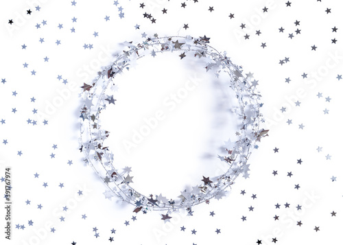 Christmas layout. A round frame made of glittering garlands is decorated with confetti in the shape of stars. White background. New Year, winter concept. Greeting card. Flat lay, copy space.