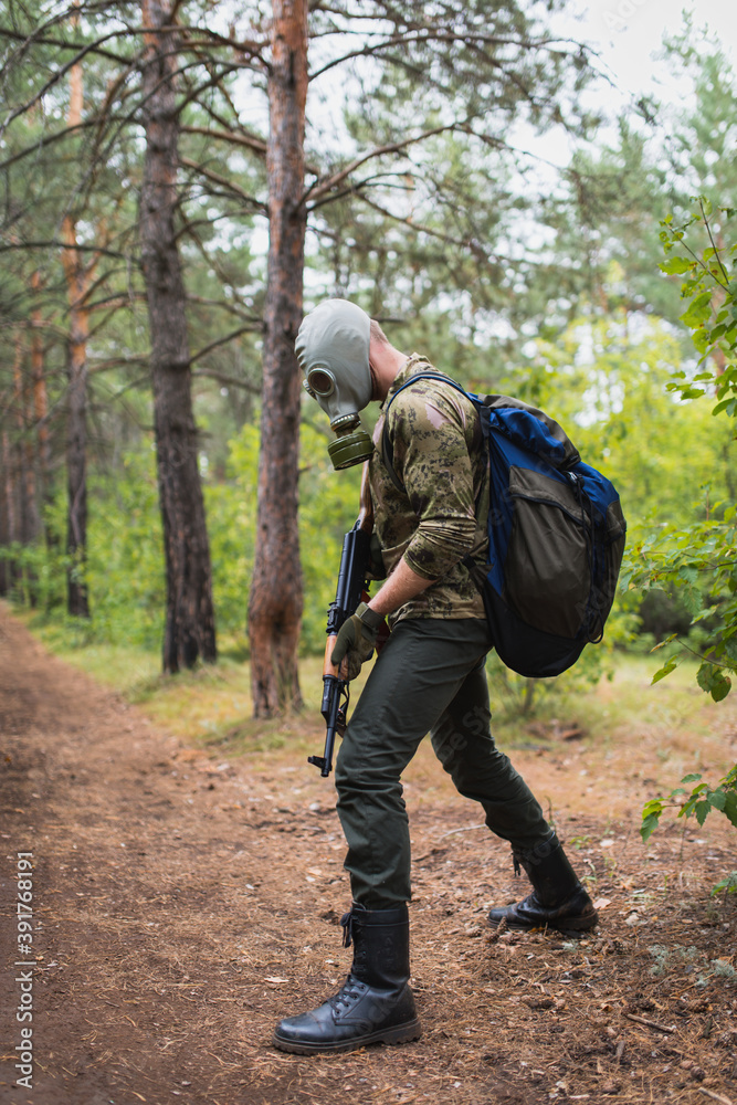 an armed soldier in a gas mask walks through the forest and tracks down the enemy