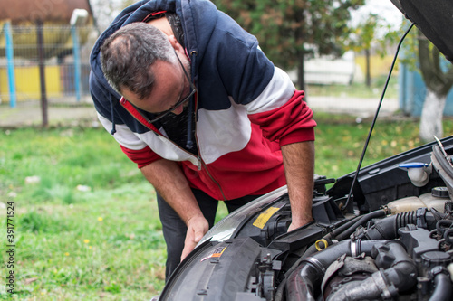 A man is trying to repair his damaged car. The car has a raised hood.