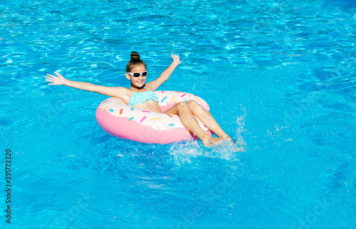 Cute smiling little girl in swimming pool with rubber ring. Child having fun on vacation