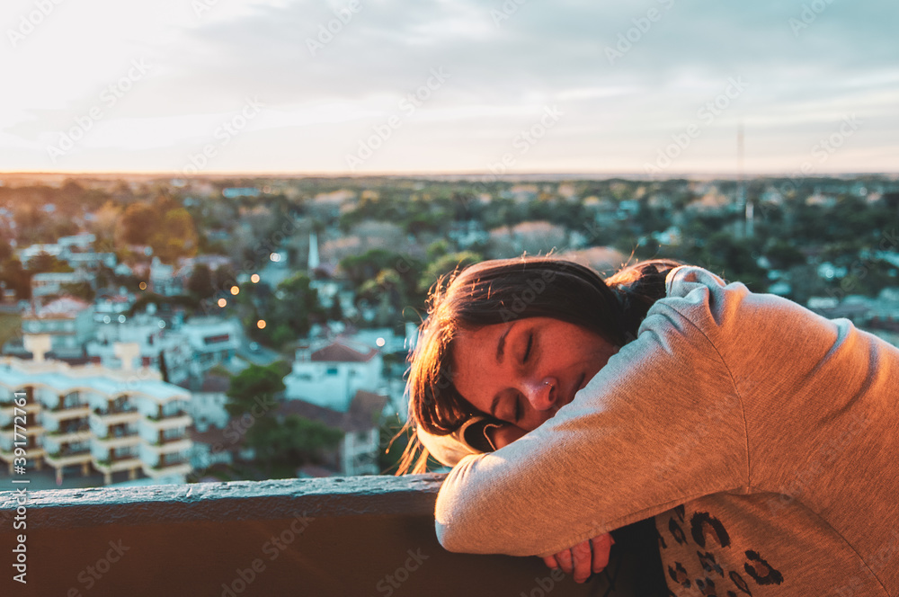 woman leaning on the edge with the city and sunset in the background
