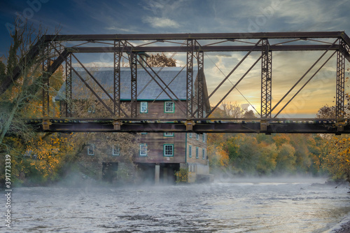 Bridge and an abandoned mill on a river with morning fog and the rising sun. 