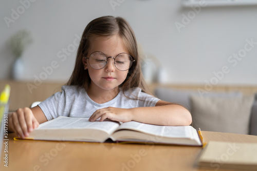 Portrait of happy small pupil learning at home. Smiling little child girl enjoying doing lessons in living room. Smart kid schoolgirl looking at camera