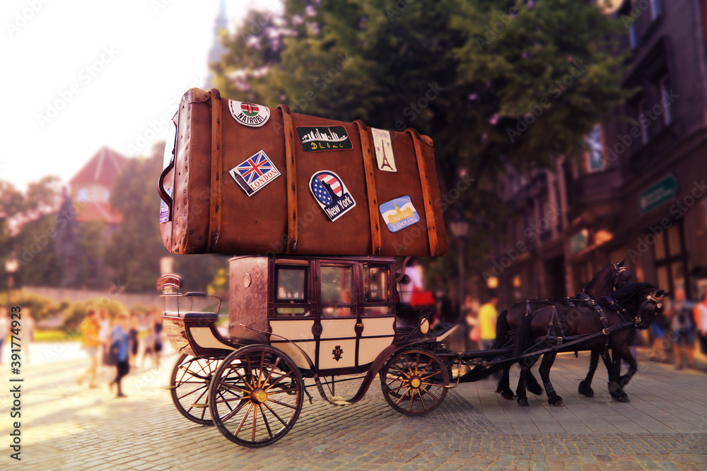 Huge suitcase of the tourist with labels of the different countries on a roof of carriage with two horses