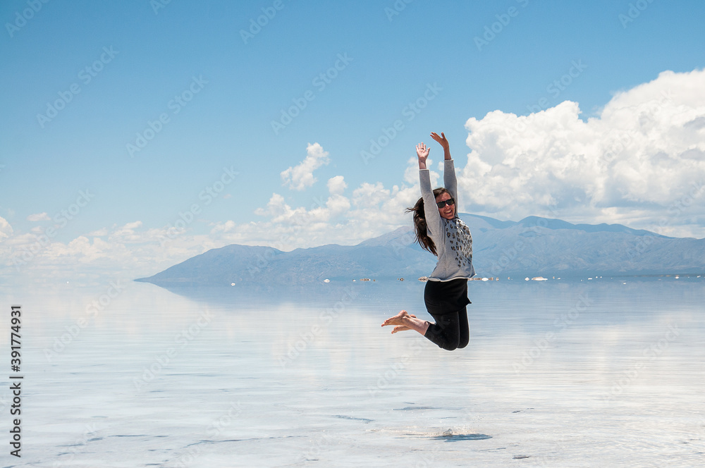 summer vacation woman happily jumping in the salt flats with blue sky, clouds and water summer vacation woman happily jumping in the salt flats with blue sky, clouds and water
