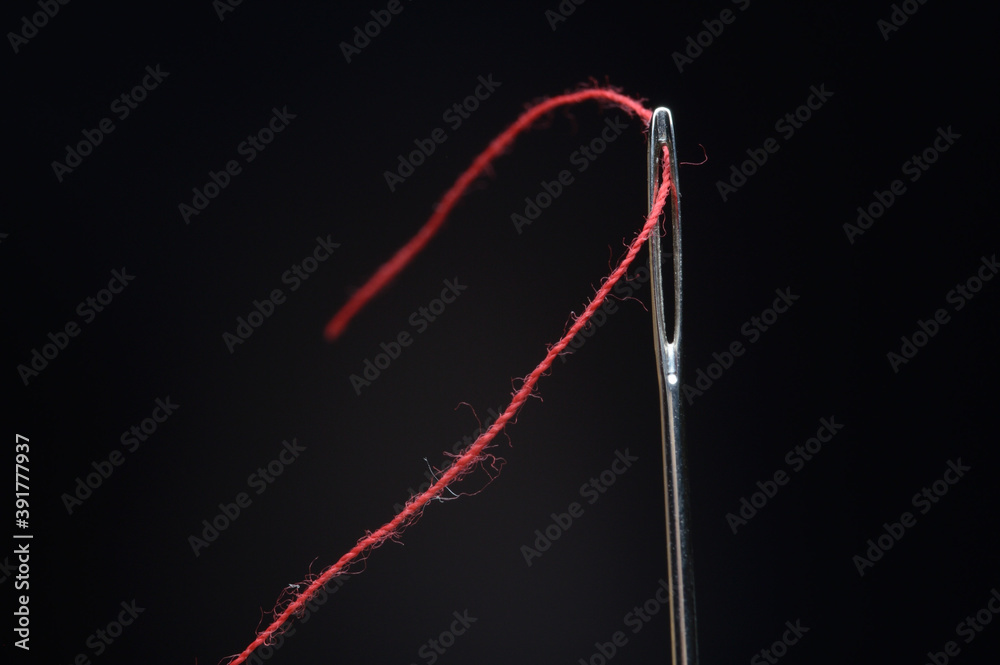 Needle and red thread on black background Needle and red thread on black background