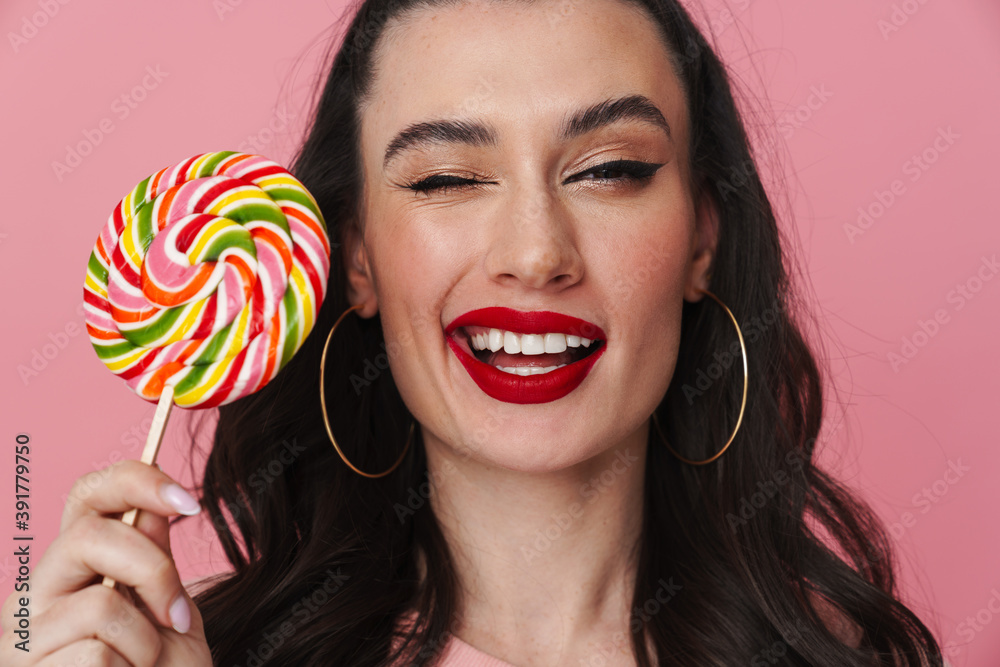 Joyful beautiful brunette girl winking and holding lollipop