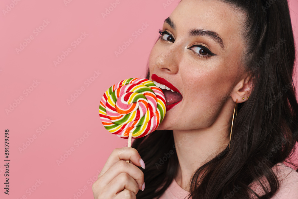 Happy beautiful brunette girl smiling and liking lollipop