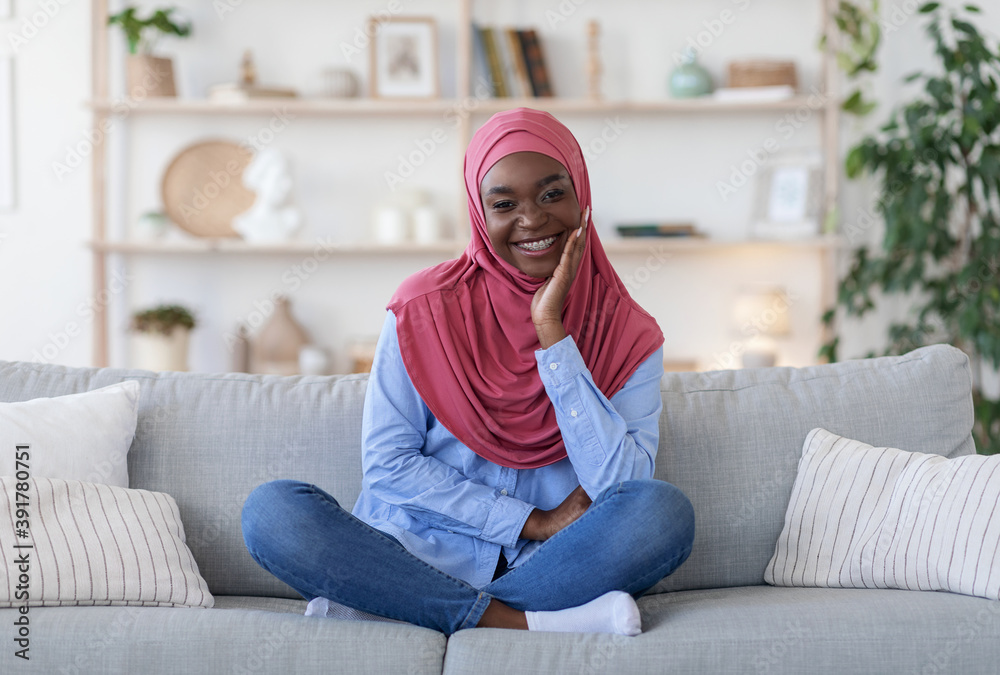 Traditional Black Muslim Woman In Hijab Posing On Couch At Home Traditional Black Muslim Woman In Hijab Posing On Couch At Home