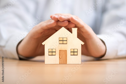 Wooden toy house protected by hands. Home insurance concept photo