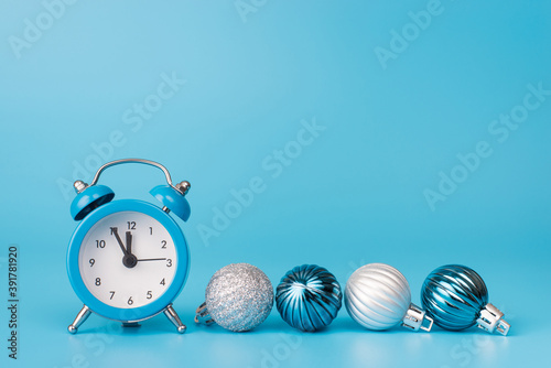 2021 is coming concept. Close up photo of light blue alarm closk with small baubles beside isolated on blue background with copyspace photo