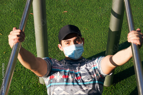 Man using his face mask doing pull ups in the park/gym