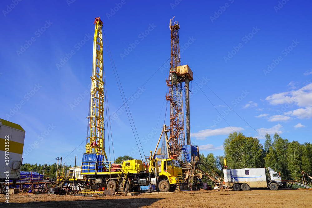 In a row are oil-producing wells. In the background, work is underway to overhaul the well. Drilling rig for drilling oil and gas wells with various equipment and materials. In a row are oil-producing wells. In the background, work is underway to overhaul the well. Drilling rig for drilling oil and gas wells with various equipment and materials.