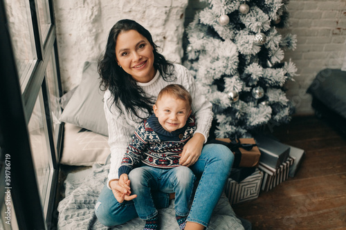Happy mother with son sit on windowsill near Christmas tree and gift box. © Stanislav