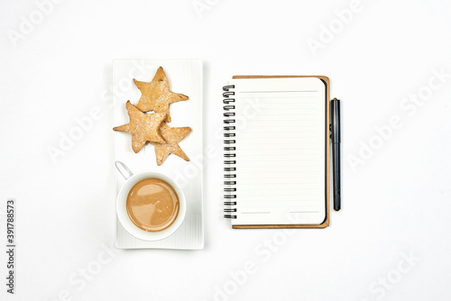 Having breakfast in Christmas morning. Drinking coffee with cookies at work. Bright working space with notepad, coffee mug and star shape cookies