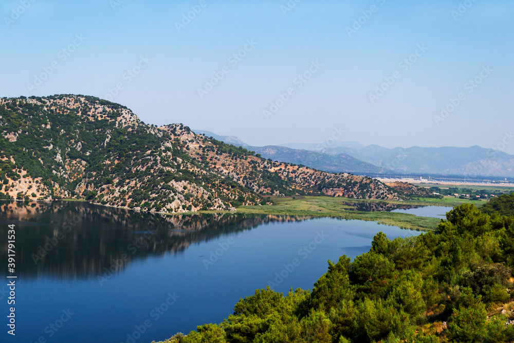 A bright blue lake surrounded by mountains, green foliage and bright blue sky in Mugla, turkey